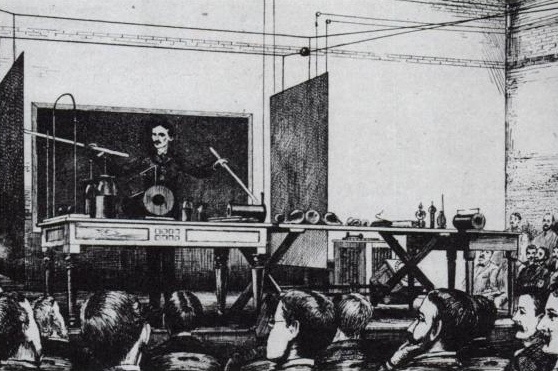 Illustration of Nikola Tesla at the front of a room demonstrating to crowds by pointing at equipment using sticks.