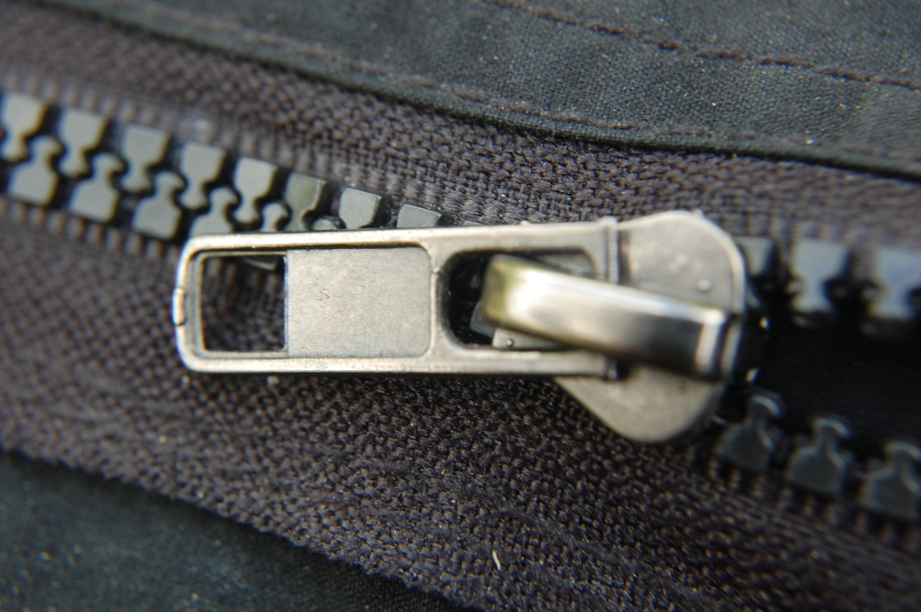 Photograph of a black zipper holding together black denim fabric, halfway unzipped.