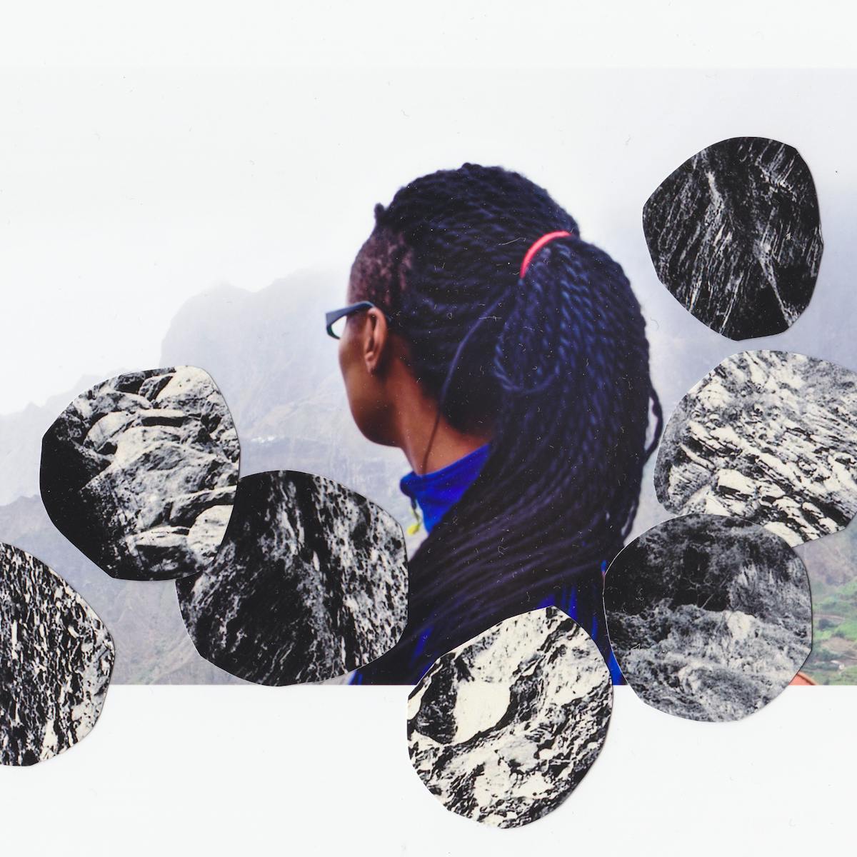 Mixed media collage artwork using a combination of two different photographic prints. The background of the collage is made up of a colour photograph of the back of the head and side profile of a young woman with long black hair, wearing glasses and a blue top. She is looking off away from the camera to the left, into the distance. Behind her is a misty view of a mountain range and green valley. Overlaid on top of this scene are cut out, irregular circular elements each of which is made up of a black and white image of rock formations. The circular pieces are placed like boulders cascading downwards.