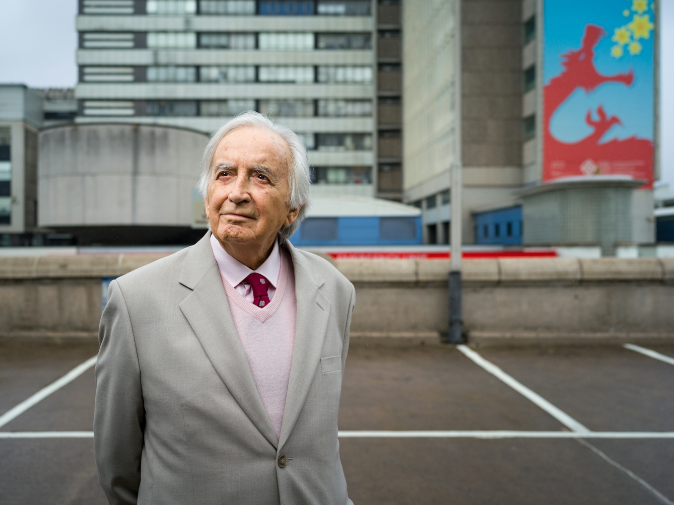 Photographic portrait of Morgan David Enoch standing in front of University Hospital of Wales. 
