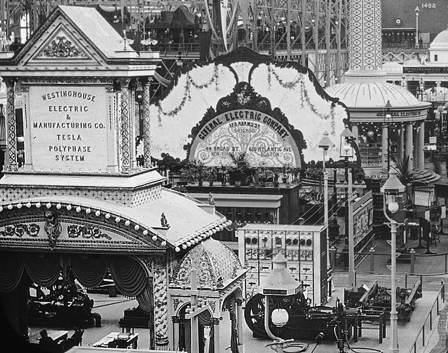 Black and white photograph of Tesla's stand at the 1893 World Columbian Exposition in Chicago showing a grand stage with various pieces of electrical equipment beside it.