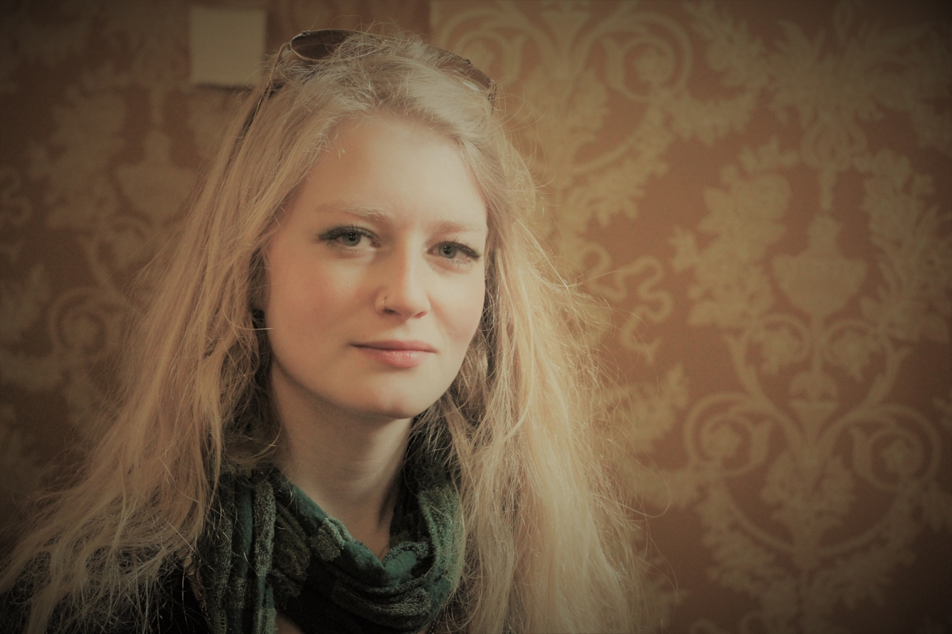 Photographic head and shoulders portrait of a young woman against a patterned background.