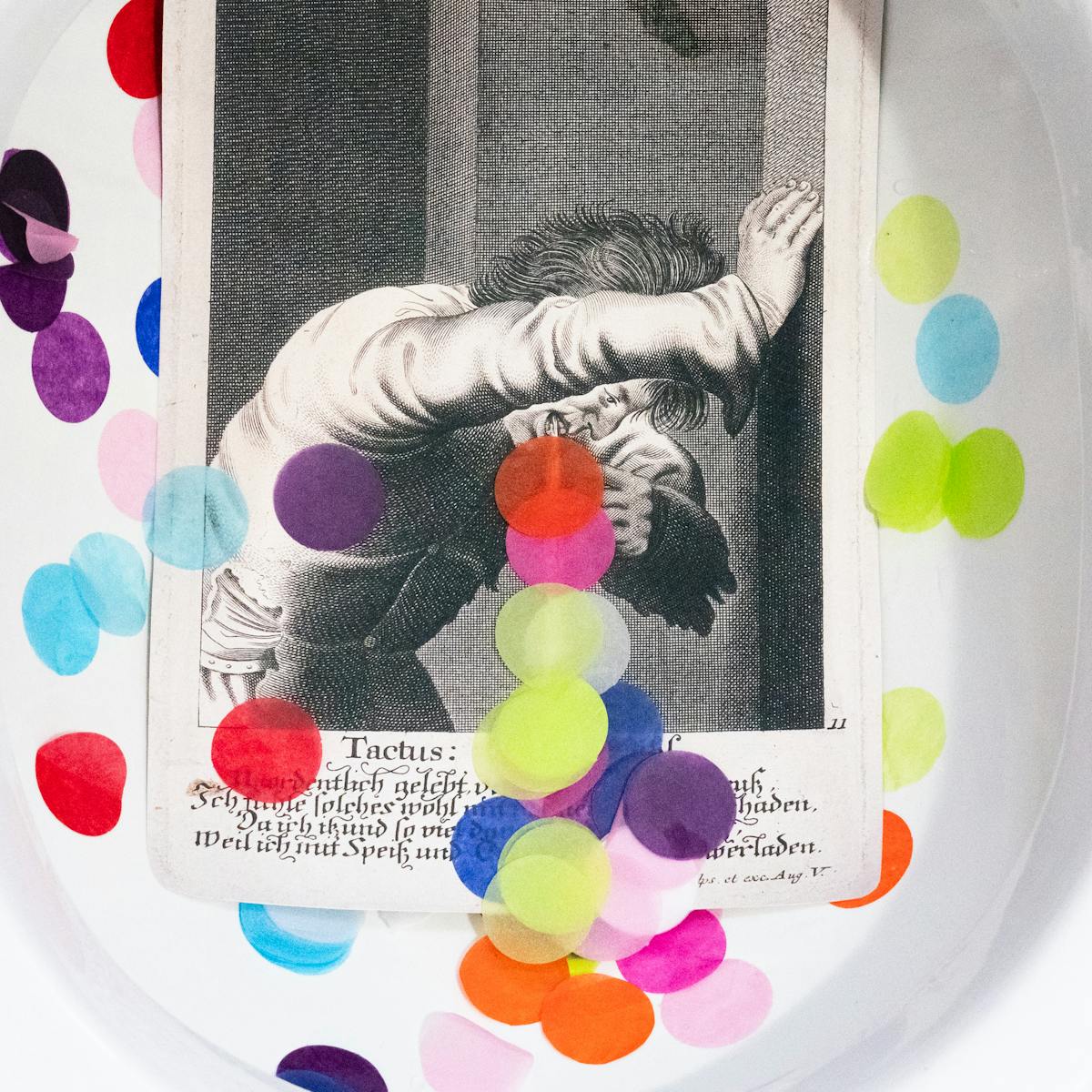 A photograph of a toilet bowl containing an illustration of a man vomiting, with multicoloured circles taking the place of the vomit.