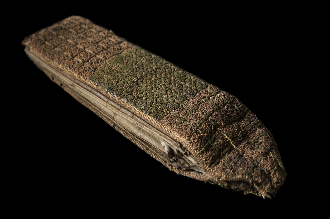 Photograph of a closed 15th century Medieval folding almanac. The binding is embroidered green and pink silk. 