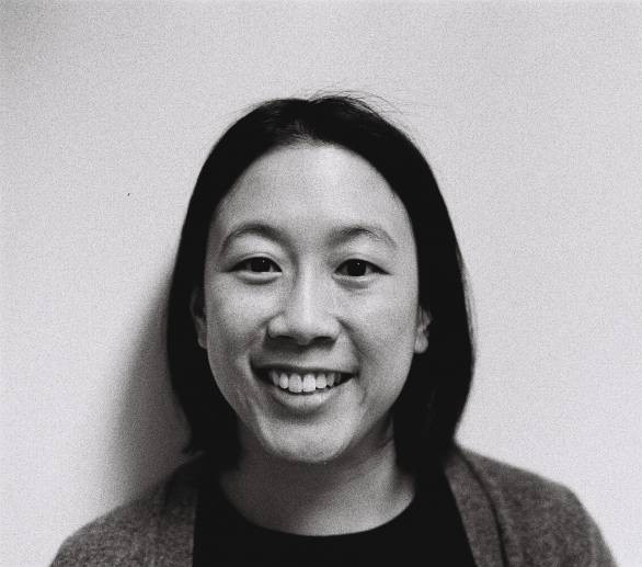 A black and white photograph of a South Asian woman looking directly at the camera and smiling.