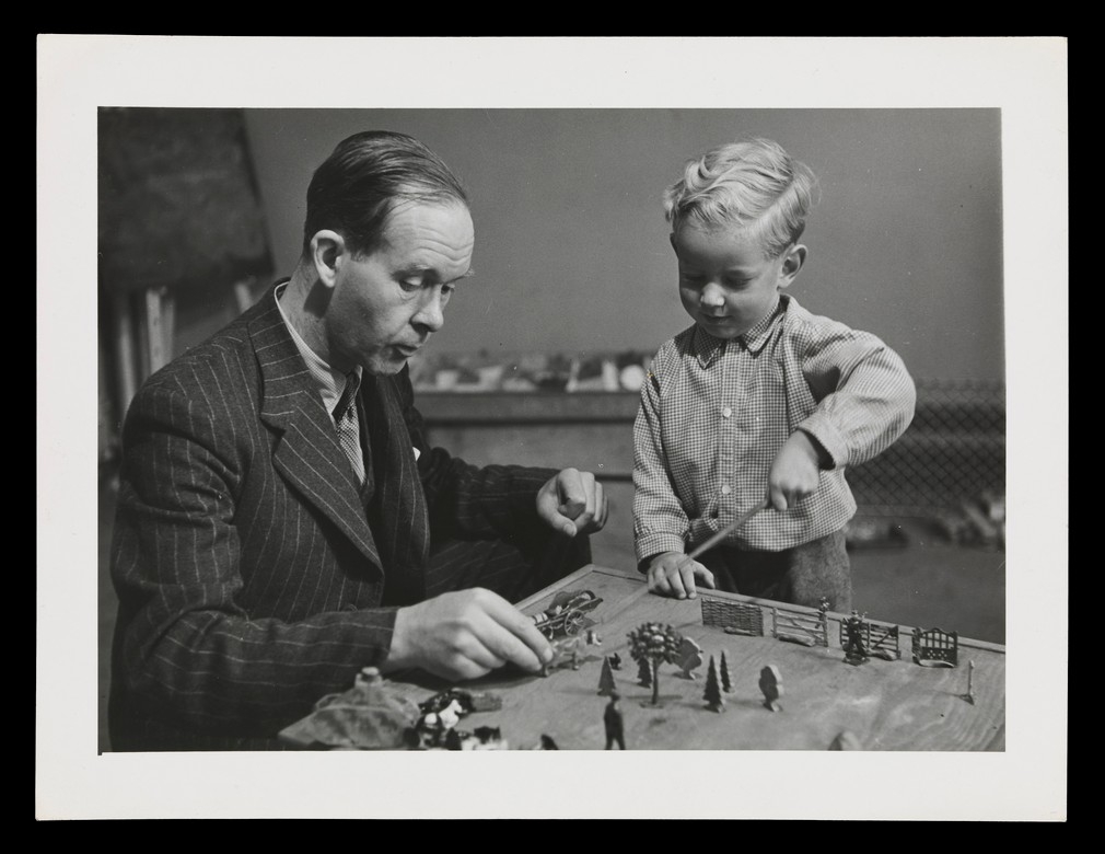 Photo with thick frame of a boy playing with small animal figurines and a man with a comb-over next to him.