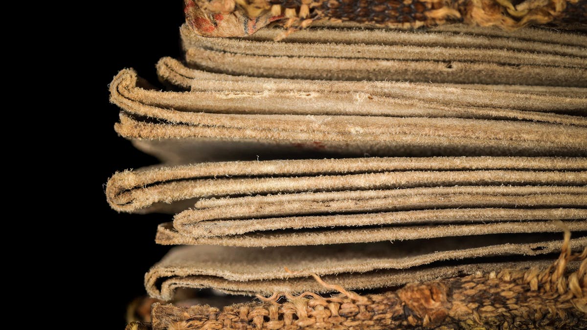 Photographic detail of a fragile folding almanac from the 15th century. The almanac is photographed from the side on a black background. It is photographed extremely close up so that the folds of the inside pages can be seen, zig-zagging back and forth. The fibres which make up the pages can clearly be seen.