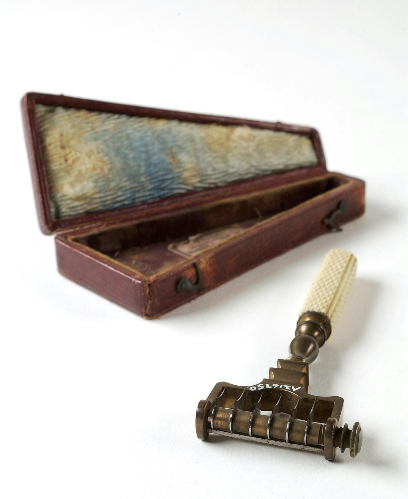 Colour photograph of a device called a scarificator beside its wooden box. The scarificator looks a bit like a safety razor with an ivory handle, but has lots of sharp blades ready to spring out and cut the skin.