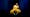 A still from a colour film. The image shows an individual in bright yellow trousers and jacket, sat on a chair with their left elbow resting on the arm rest, hand raised up by their face. They are looking to camera with a questioning tilt and expression to their face. Behind them is a black and blue background. They look as if they may be sat on a stage of some kind.