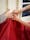 A photograph in portrait orientation showing a close up of a large piece of red fabric being held up against a magnolia painted wall by three hands, one of which belongs to a young person, the others a child. Parallel to one another are two pipes painted magnolia running up the wall, and in the top right of the image the bottom corner of a blacked out window can be seen.