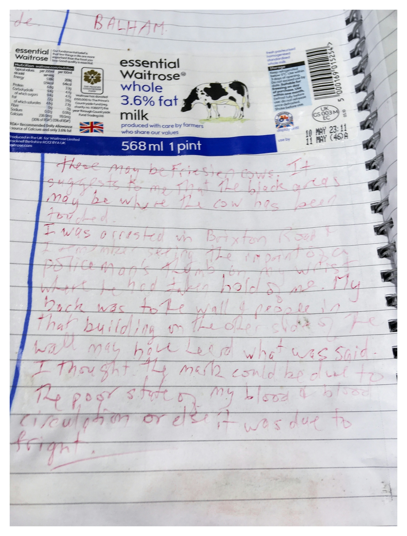 Documentation photograph of a page from a lined scrapbook. At the top is a stuck-in label from a milk bottle including a drawing of a Friesian cow. Below the label is a long handwritten passage which discusses how the black areas of the cow remind the writer of a violent personal experience.
