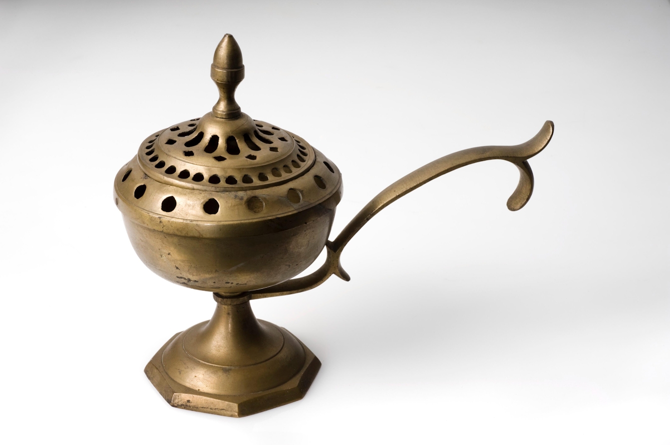 Photograph of a brass goblet covered by a perforated lid, with a long decorative handle.
