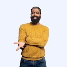Portrait of Dr Alex Lathbridge wearing a yellow jumper and holding his hand outstretched palm up in a questioning pose.
