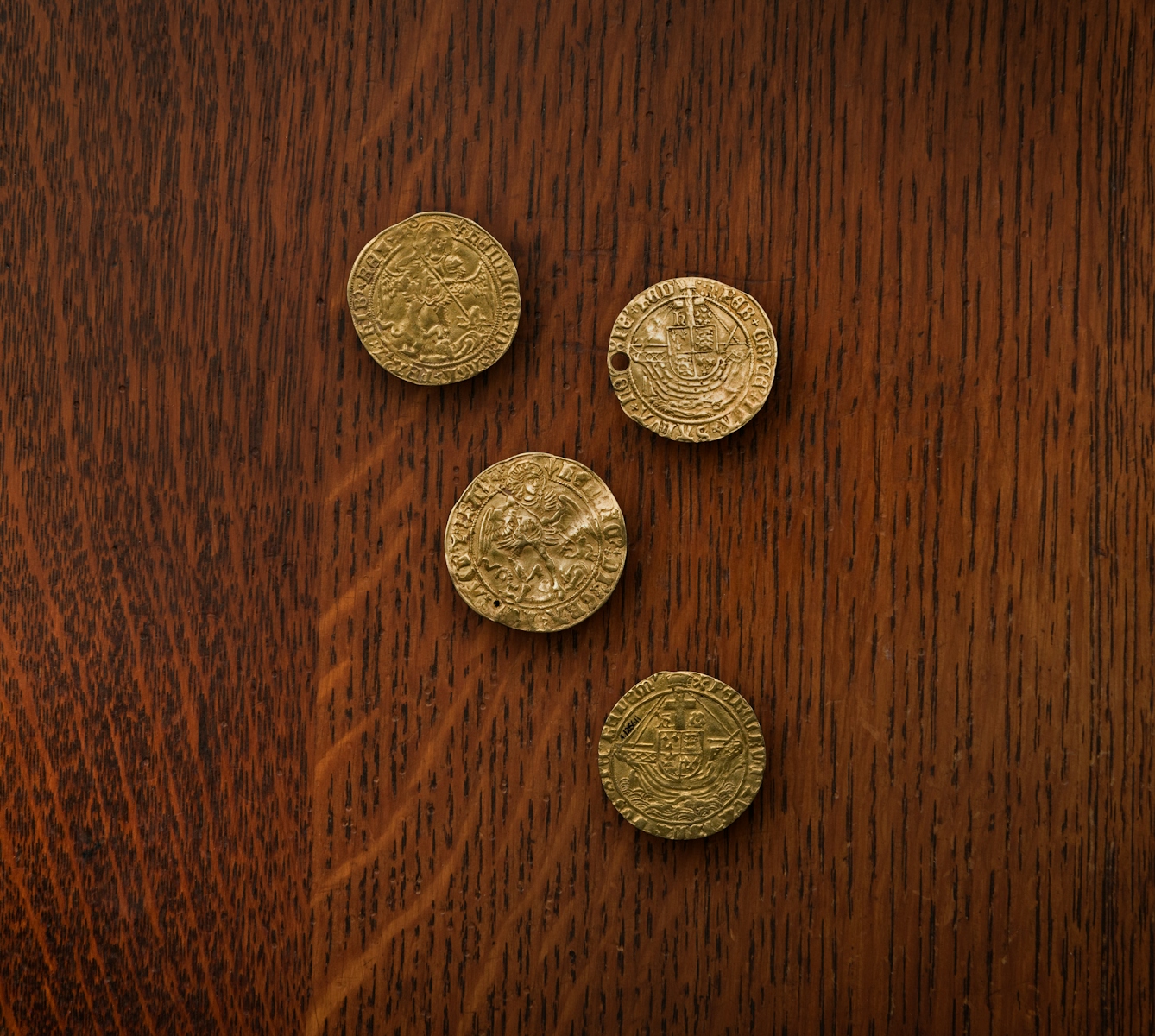 A photograph of four gold coin touch pieces, each coin has markings around its edge and across its face, one of the coins is punctured with a hole.