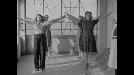 Image of women standing in two lines with their arms stretched upwards.