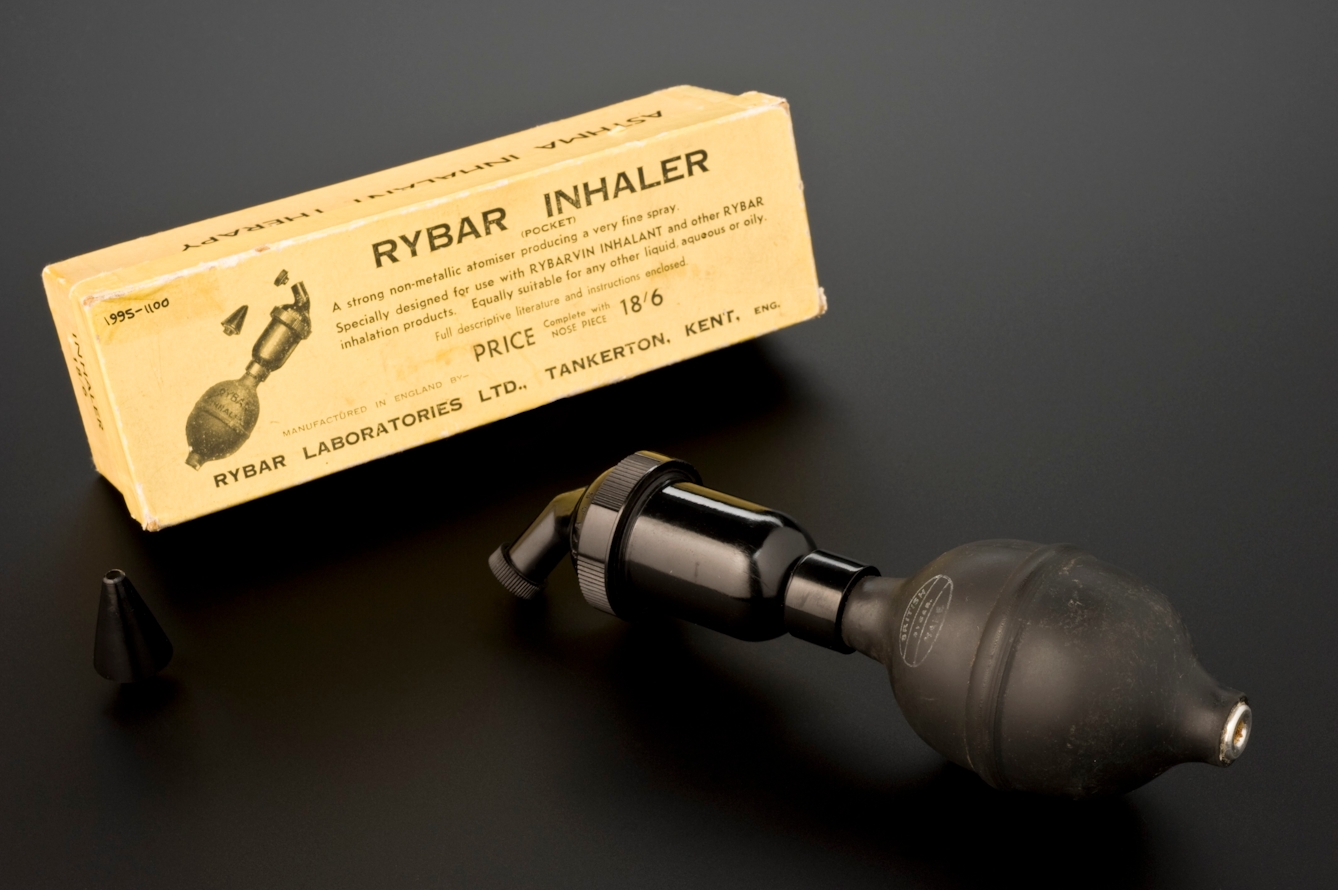 A "Rybar Inhaler" beside the yellowing box it was originally packaged inside. The inhaler has a rubber bulb attached to a metallic-looking tube.