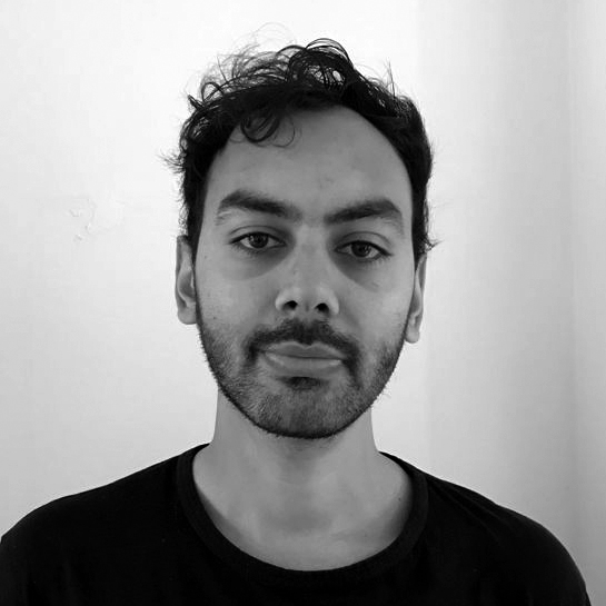 Head and shoulders photograph of a man with tousled hair and a short beard, wearing a black t-shirt