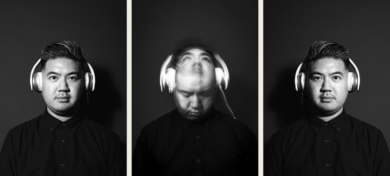 Photographic triptych showing in the centre, a black and white photographic portrait of a man dressed in a black shirt wearing a pair of over ear headphone with the white cables trailing over his shoulder. He is pictured from the chest up. The man's face is spotlit in a small circle of light. He is standing against a black background which means he is surrounded by darkness. He is moving his head up and down causing his head to motion blur in vertical line across the image. A flash light has caught this head as it faces up and down, creating a sharp image within the blur. The images on the left and right are a mirror image each other and show the same man in the same scenario, but looking straight to camera without any movement.
