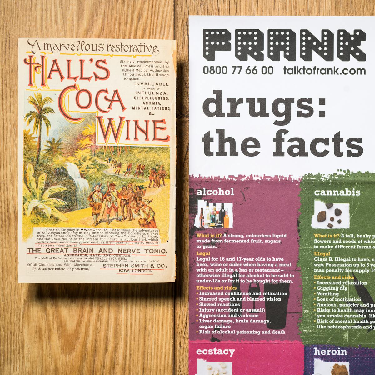 Photograph showing two items of ephemera from the Wellcome library. Photographed on a  wooden table, one item is promoting Hall's Coca Wine and reads "A marvellous restorative". The other is part of a drug awareness poster from the 1980/90s titled "Frank, drugs: the facts".