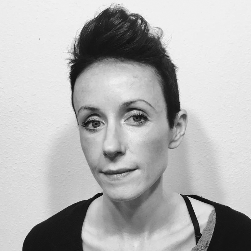 Head and shoulders photograph of a young woman with her hair in a a quiff, wearing a dark top.