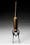 Photograph of a brass enema syringe standing vertically on a background that graduates from white at the bottom of the frame to black at the top.