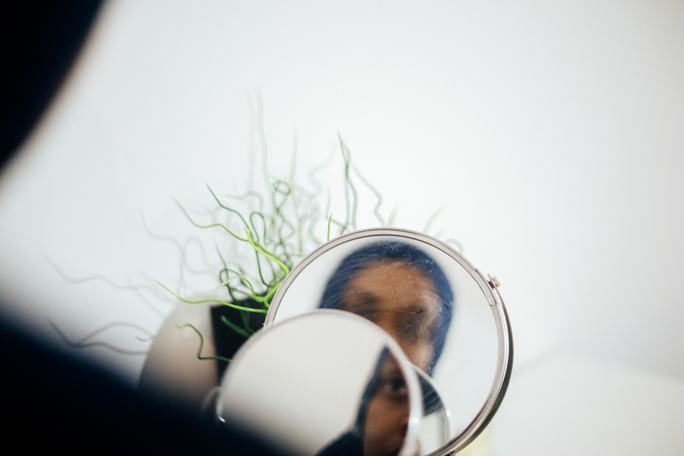 Photograph of a woman looking into circular mirrors. In the reflection you can see her face, out of focus.