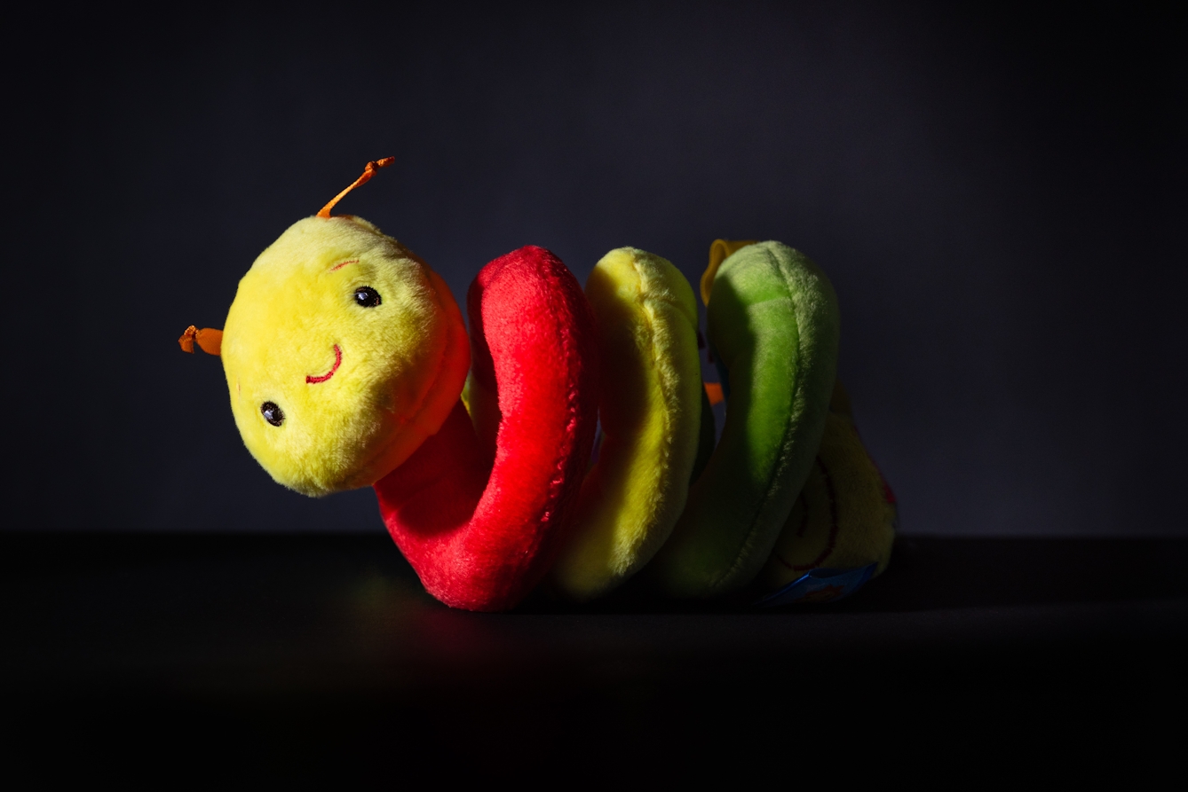 A photograph of furry toy against a black background. The body of the toy is a multi coloured spiral and appears so that one half is in dark shadow and silhouette.