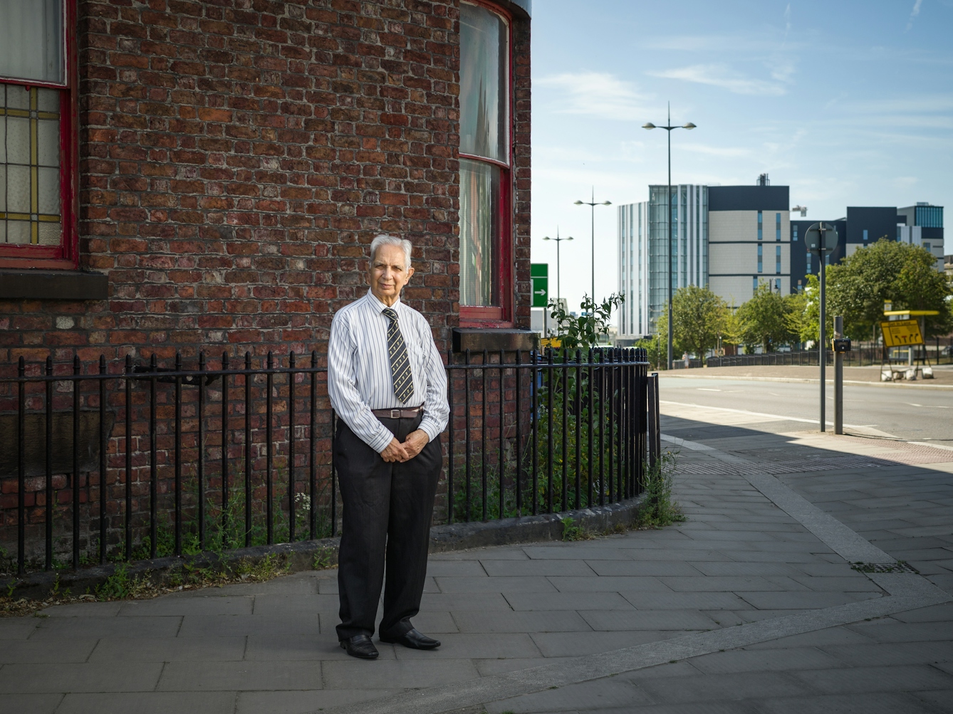 Photographic full length portrait of Dr Shiv Pande, a retires general practitioner, outside his former surgery in Liverpool.