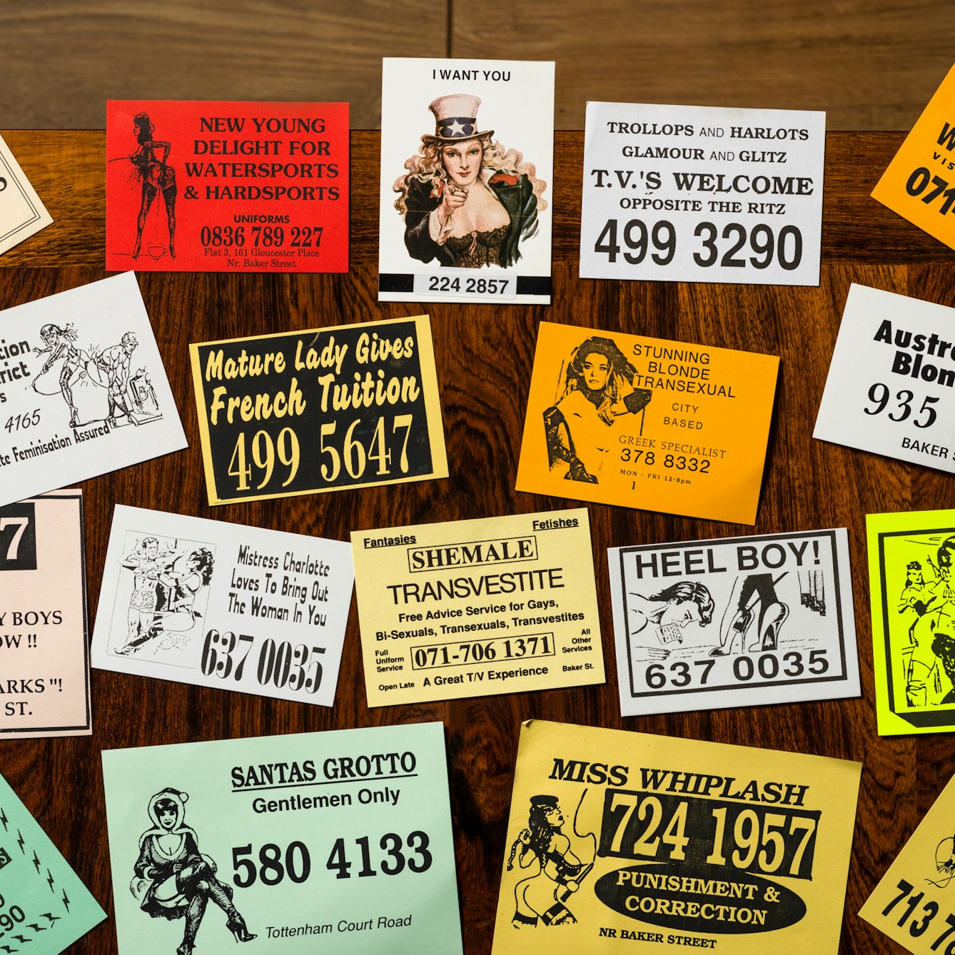 Photograph of a selection of cards from the sex worker card collection at Wellcome Collection, laid out on a wooden tabletop.