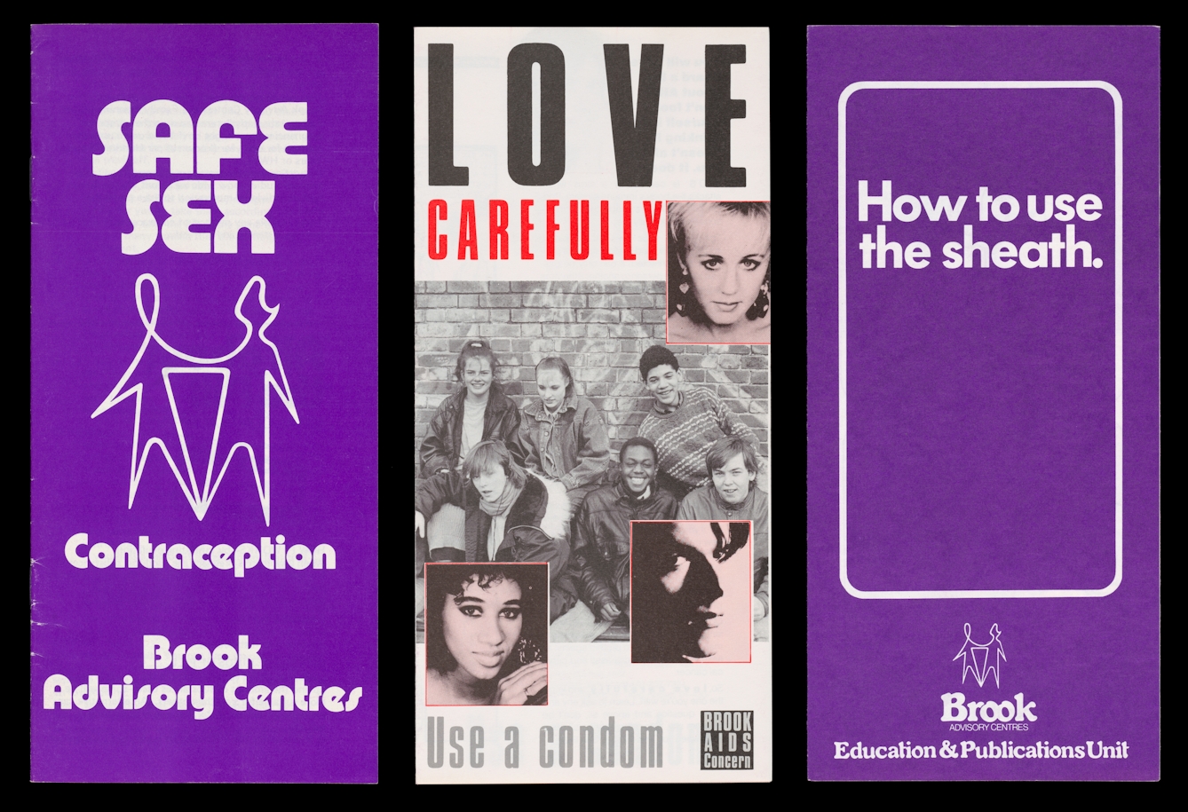 Photograph of archive material from the 1980s against a black background. The image shows 3 DL size leaflets, side by side. The leaflets to the left and right are a purple colour with white text and graphics. The one to the left carries the words 'Safe Sex, Contraception, Brook Advisory Centres'. In the centre is an abstract line sketch of two people holding hands. The one to the right carries the words 'How to use the sheath' within a rounded edged rectangular white line. The leaflet in the middle show a black black and white photograph of a group of young people looking to camera, with 3 smaller red tinted portraits of young faces, overlaid onto of the first larger image. Surrounding the images are the words 'Love Carefully, Use a condom', with a small logo for the Brook Advisory Centres.