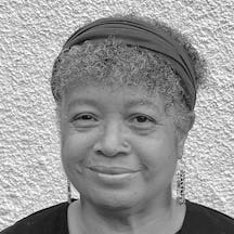 Black and white photograph of the head and shoulders of a middle aged black woman with shor hair. She is smiling and looking directly at the camer.