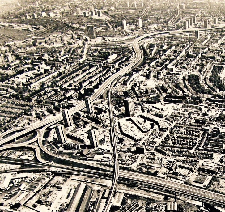 An aerial photographic view of the North Kensington estates in West London. The A40 roadway cuts through the middle of the image, with four high-rise buildings in the centre