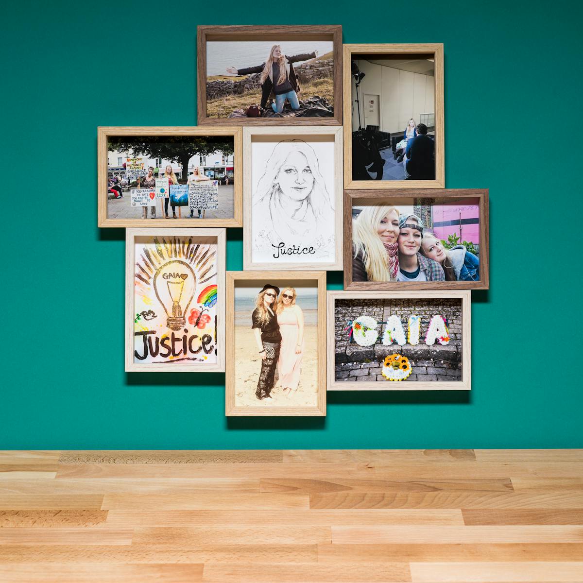 Photograph of a multiframe photo frame containing eight photographs, seven in colour and one in black and white. The frame is hung on a cyan-coloured wall above a wood block tabletop.