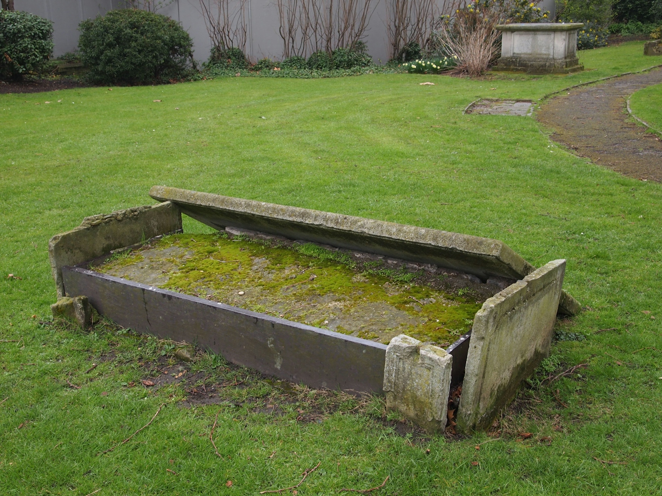 Photograph of a grave in St James's Gardens.  The stone from the top of the grave has been dislodged exposing the earth beneath it.