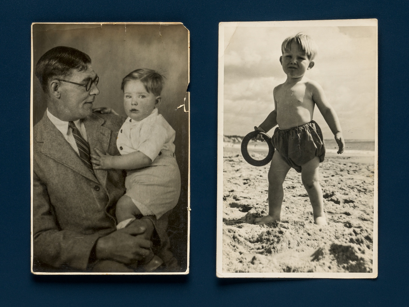 Photograph of 2 sepia toned family photos resting on a deep blue background. The photo on the left is taken in a studio and shows a father holding a young child of 2 or 3 years old. The period is the 1950s and the father wears a suit and tie and glasses. The photo on the right shows the same child, but this time on a sandy beach in sunshine, wearing a swimming costume. They are holding a hoop in one hand and looking to camera.