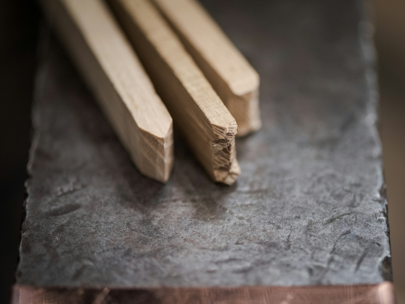Photograph of specially crafted wooden sticks resting side by side on a metal surface. Each stick will make a different impression on solidified lead. Two of the sticks used in tandem will create a cross, and the third stick will create a line.