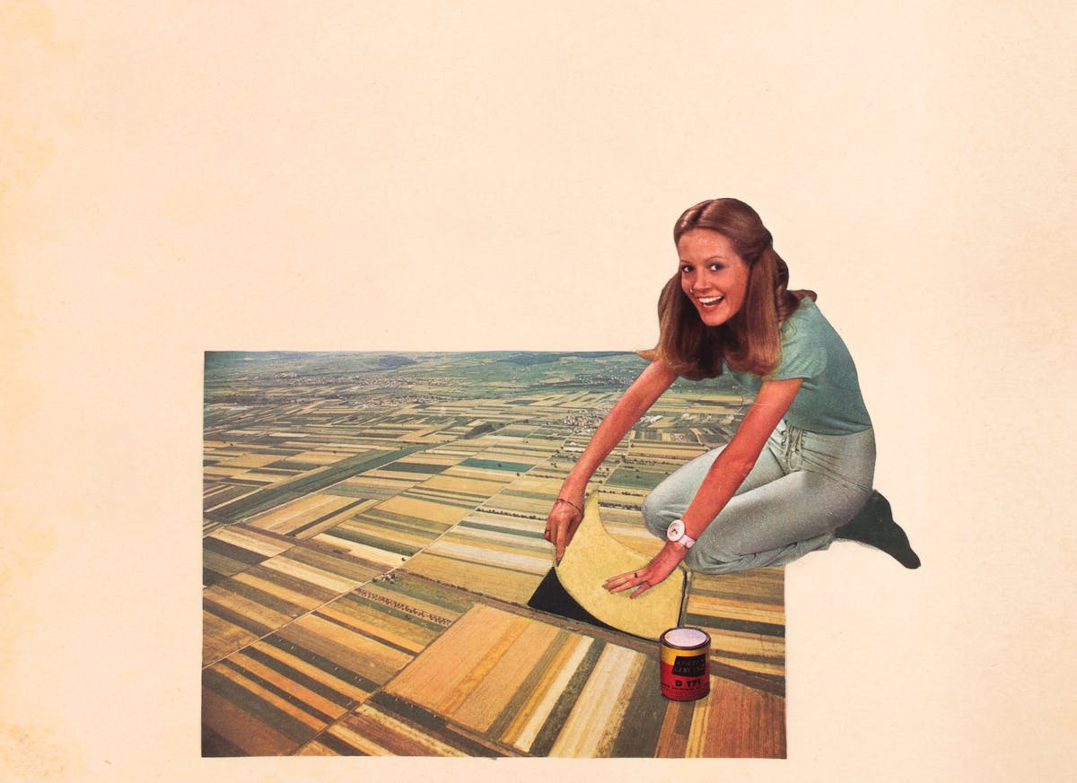 Paper collage artwork of a gigantic woman kneeling on an agricultural landscape.  The woman appears to be peeling away one of the farmers fields showing an expression that reads both as joy and mischief.