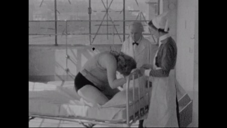 Image of woman kneeling on the end of a bed, with a nurse and doctor standing to her sides.