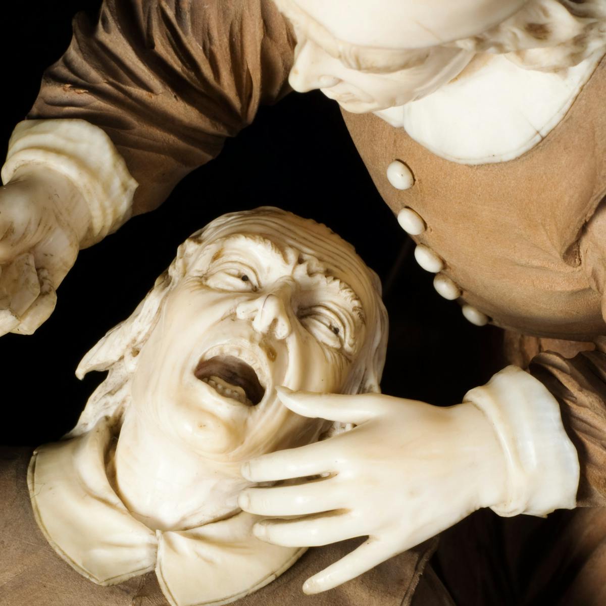 Close up photograph of a statue of a man being treated by a dentist. The patient is seated, with his head thrown back and his mouth open; the dentist is standing over him holding a dental instrument.