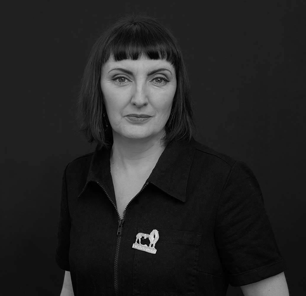 Black and white photograph of a middle-aged woman with shoulder length dark hair. The woman is looking directly at the camera with a neutral expression.