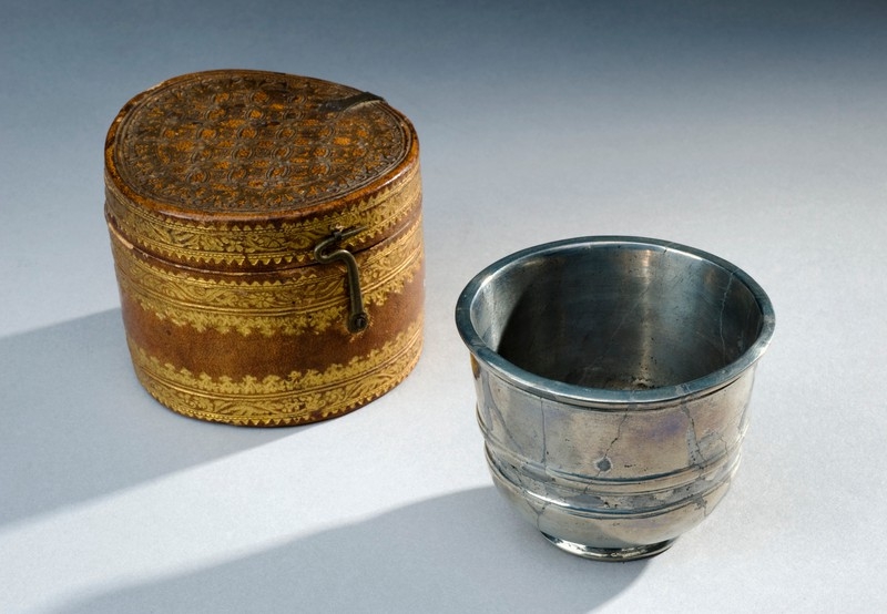 Image of small silver metal cup with an ornate leather case next to it.