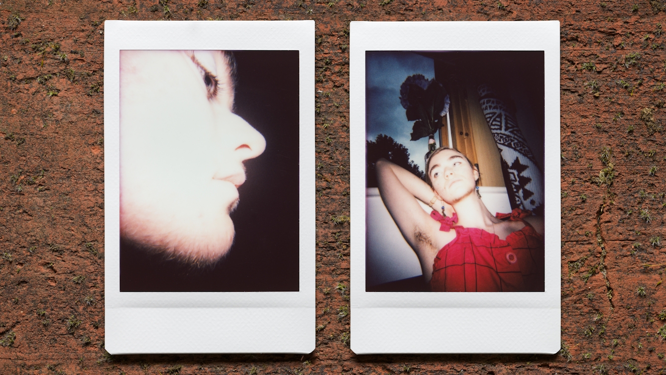 Photograph of two Instax Mini instant film prints in a line, resting on a textured brick surface. The two prints feature the same woman. The print on the left shows a close-up of her face, slightly bleached out by the camera flash. Hair can be seen growing on her chin and upper lip. The print on the right shows her reclining against a window with a view to the outside world behind her. She is wearing a red top and has her right arm raise behind her head to show her armpit hair.