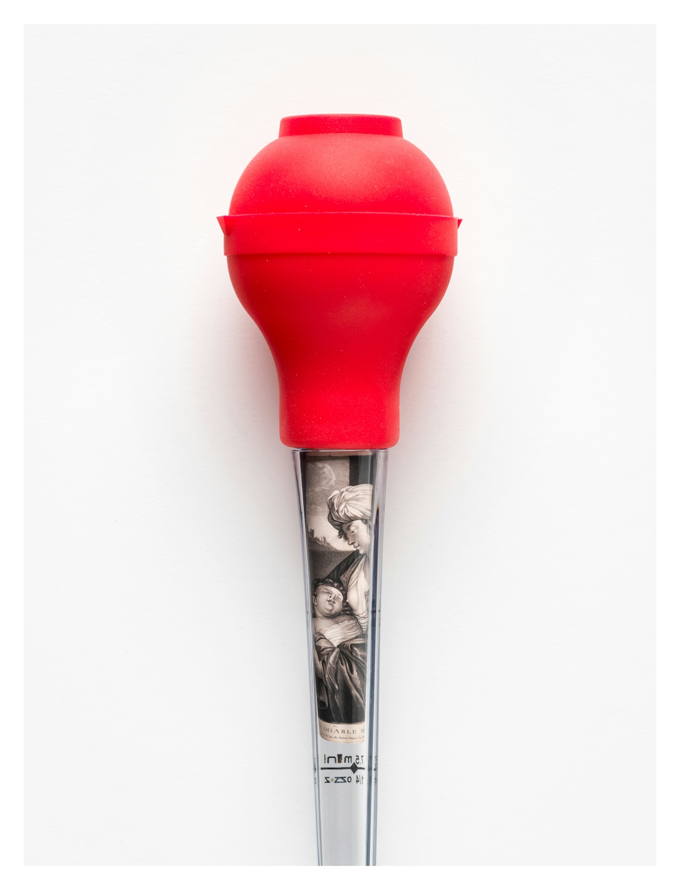 Photograph of a glass turkey-baster with a bright red rubber bulb, against a white background. Rolled up in the glass tube is a monotone etching of a mother with a young child in her arms. The two are gazing towards each other.