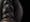 Photograph of the carved wooden head of a woman against a black background. The image shows a close-up detail of the elaborate headdress.