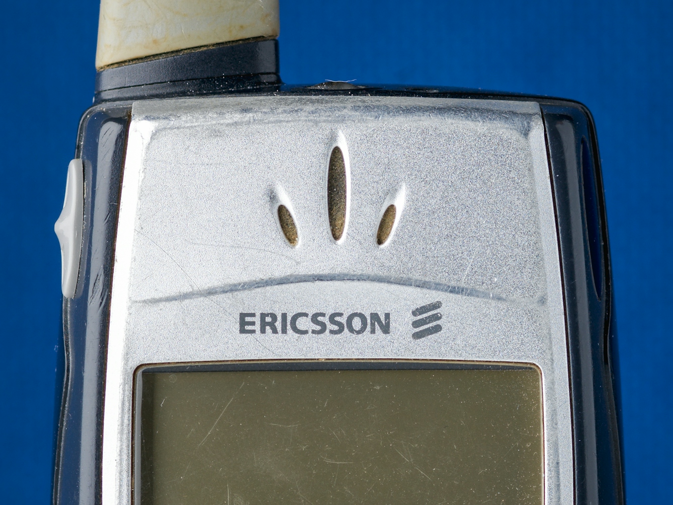 Photograph of a close up of a mobile phone's receiver earpiece, against a blue felt background.