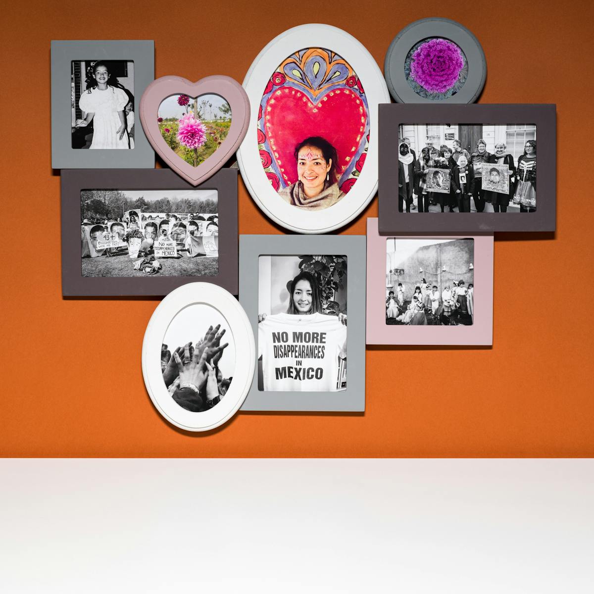Photograph of a multiframe photo frame containing nine photographs, three in colour and six in black and white. The frame is hung on a brown wall above a white tabletop.