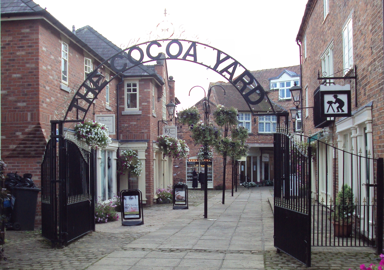 Colour photograph showing the entrance to The Cocoa Yard in Cheshire, with a metal sign arching over the gap.