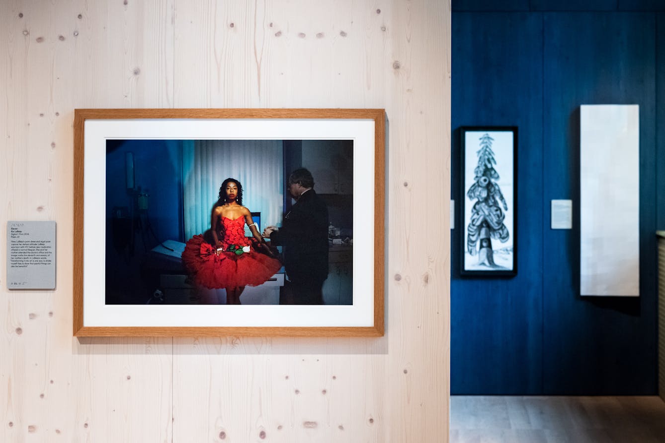 Photograph of a gallery wall showing a framed photograph of a woman in bright red dress in a medical clinic.