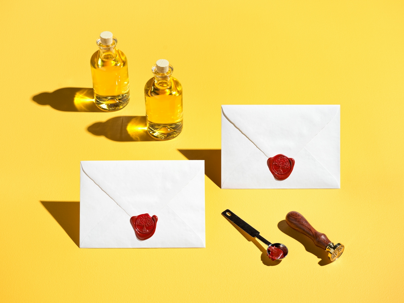 Photograph of 2 specimen bottles containing yellow liquid, 2 enveloped sealed with a red wax seal of a tree and is roots, a silver spoon and a wooden handled stamp. The whole scene has been photographed against a bright solid yellow background.