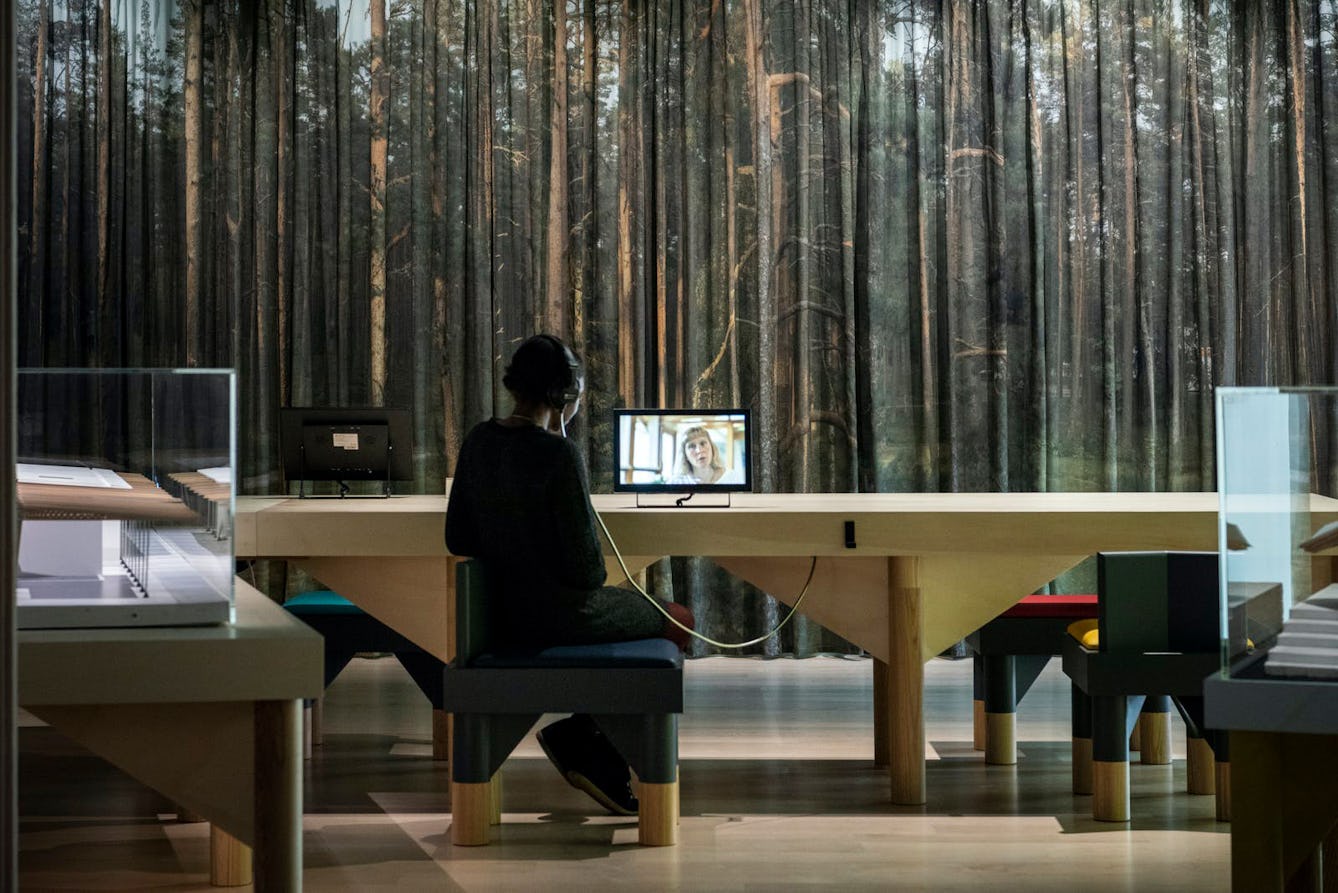 Image of a visitor watching a film on a small table mounted screen in the Living with Buildings exhibition. The angle of the screen can be adjusted to suit the visitor. There is a single seat but also space for a wheelchair to approach.
